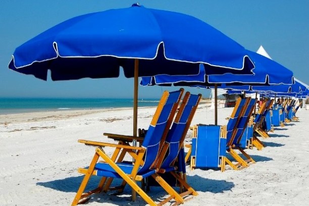 Beach with blue umbrellas and wooden lounge chairs lined up on the sand.
