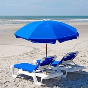Two beach chairs under a blue umbrella on a sandy beach.