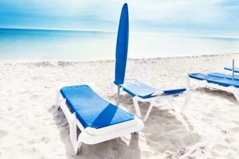 Beach with blue loungers and umbrellas under a clear sky.