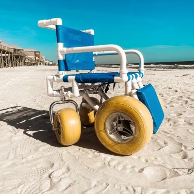 Beach wheelchair with large wheels on sandy shore under clear blue sky.
