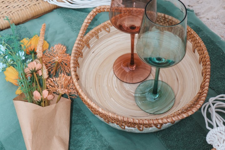 Two empty wine glasses on a basket with flowers on a picnic mat.
