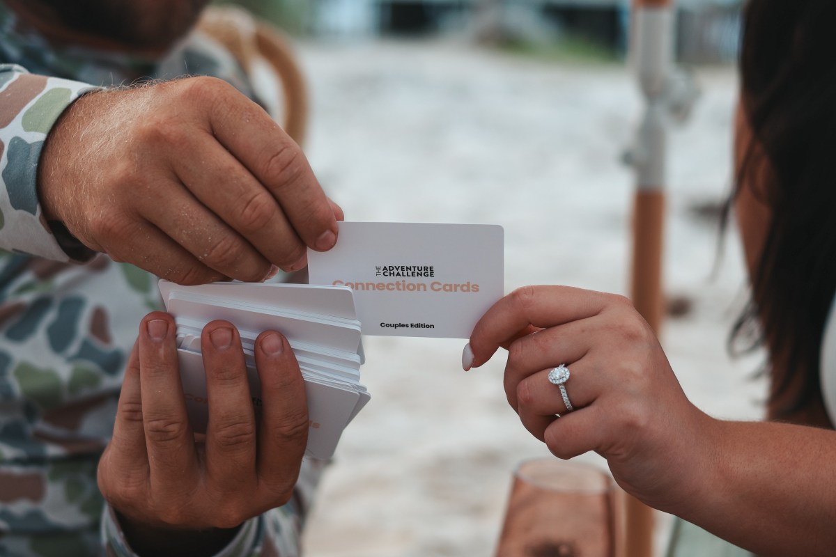 Two people exchanging a card labeled 'Connection Cards' on a beach