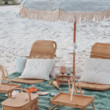 Beach picnic with chairs, umbrella, blanket, pillows, and baskets.