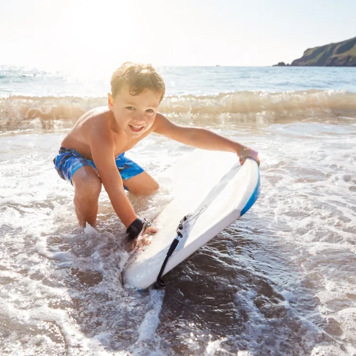 Child in blue shorts playing with a surfboard at the beach.