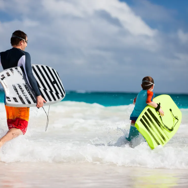 Two people in wetsuits carrying bodyboards run into the ocean.