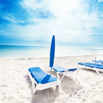 Empty beach with blue sun loungers and umbrellas under a bright sky.