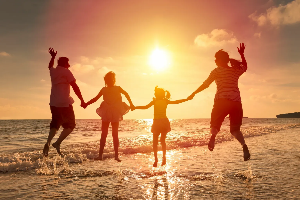 Family holding hands and jumping on a beach at sunset.